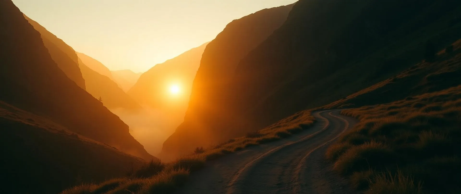 A winding mountain pathway leading toward a golden sunrise between two ridges